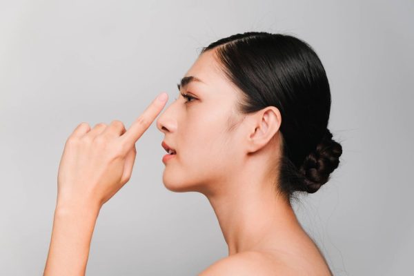 Seorang perempuan tampak samping menyentuh hidungnya, menggambarkan konsultasi operasi hidung